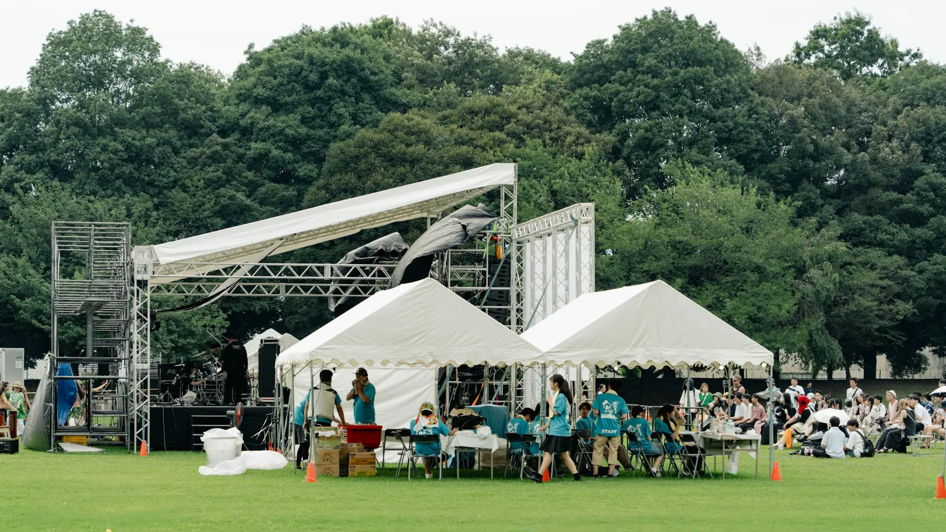 A stage and white tents set up on a park field, with people gathering.